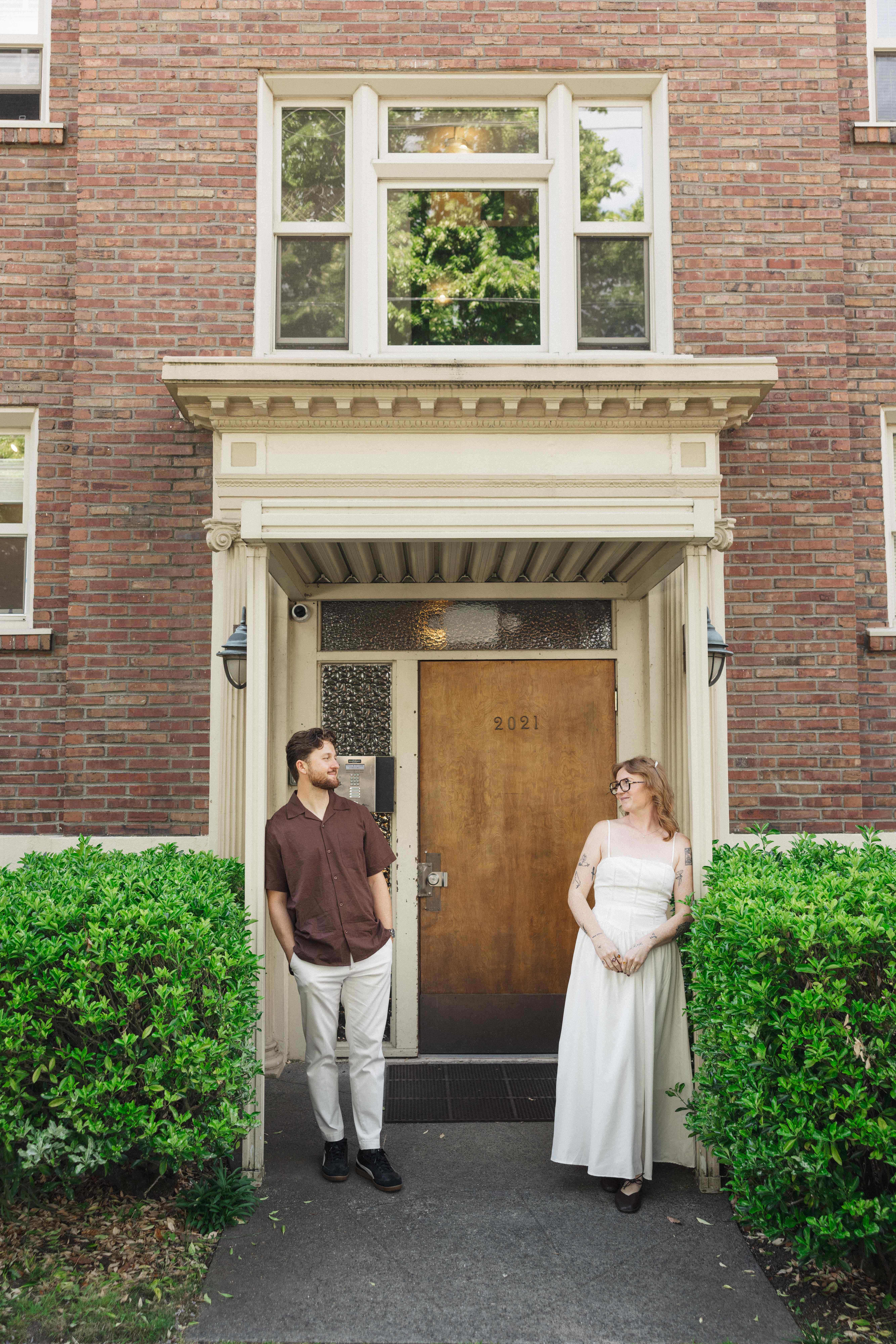 Madison and Evan standing beside a wooden doorway framed by hedges