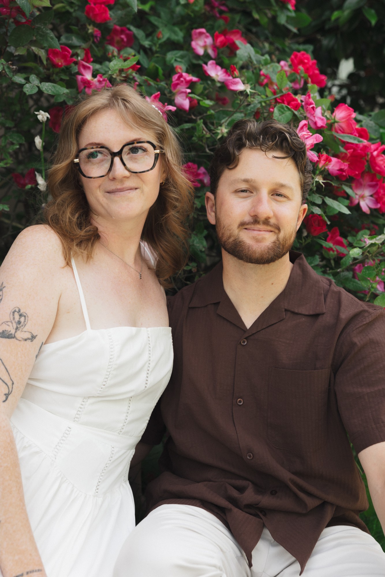 Madison and Evan sitting together in front of a blooming rose bush