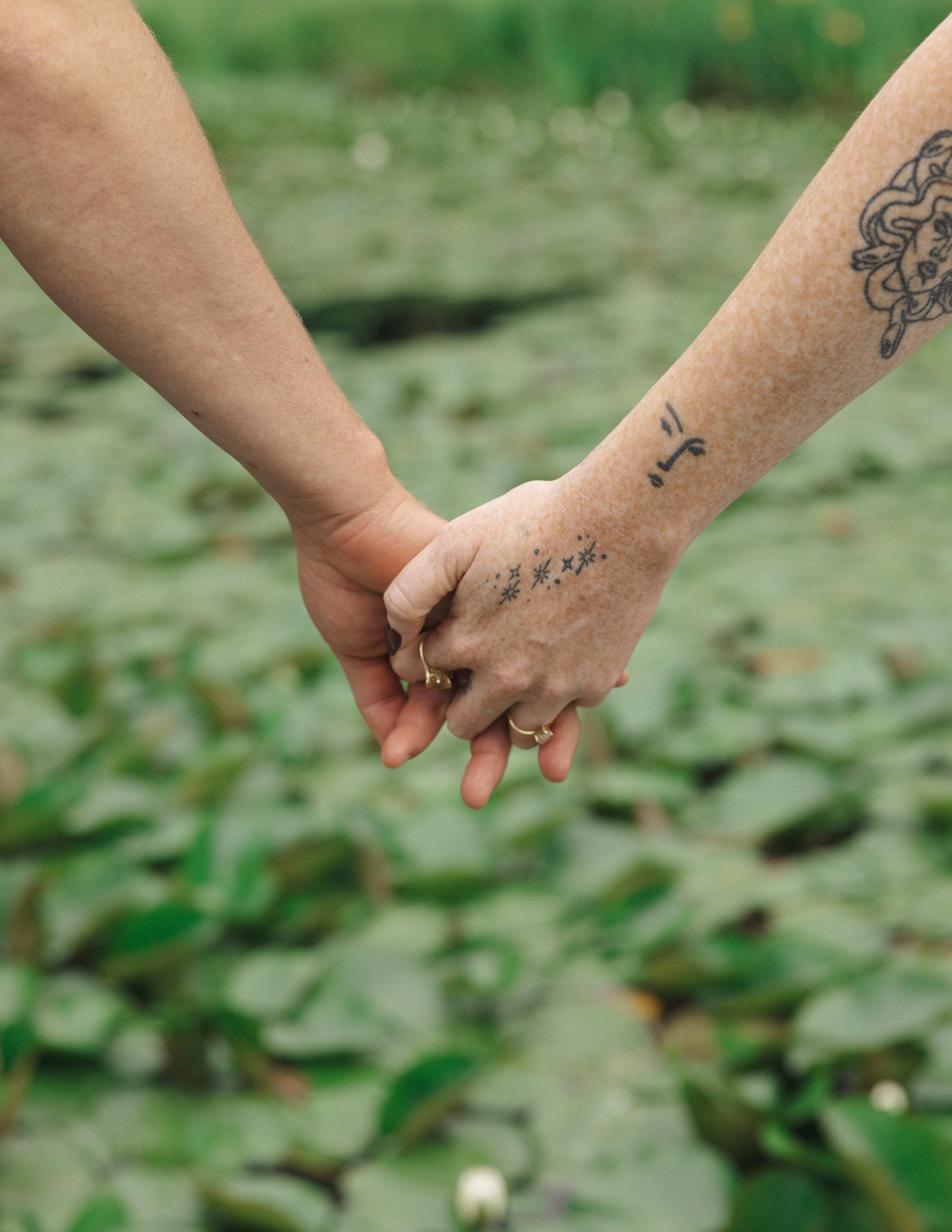 Close-up of Madison and Evan holding hands, showing their rings and tattoos