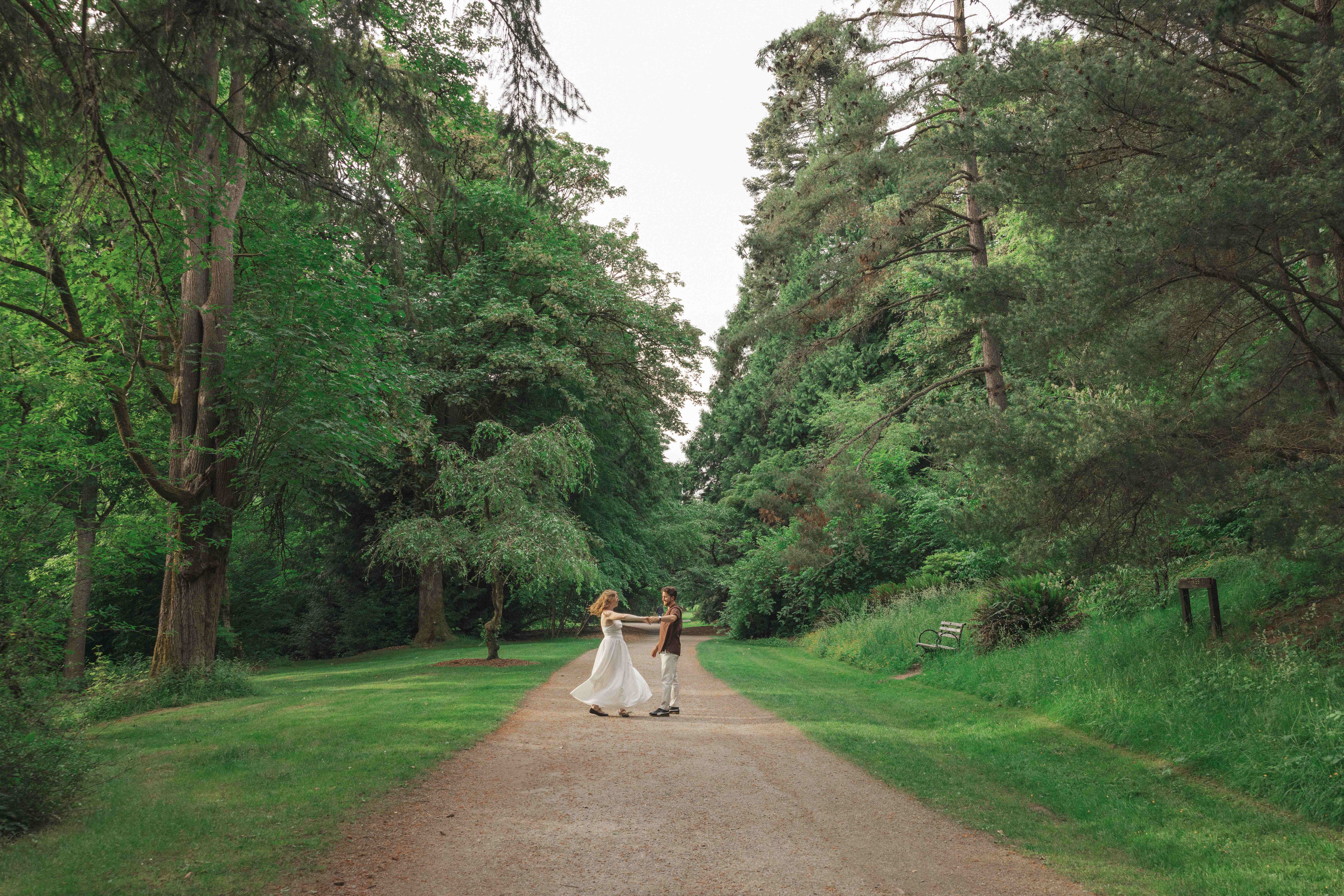 Madison and Evan dancing on a garden path lined with tall trees