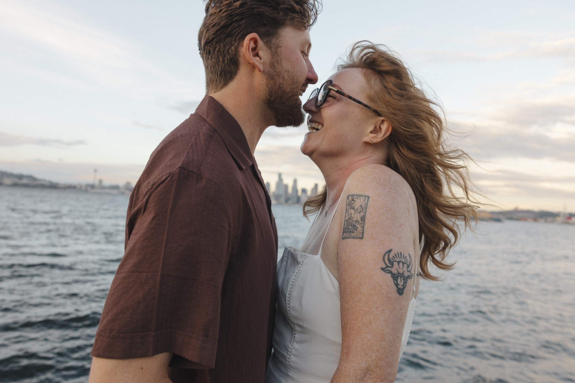 Madison and Evan laughing nose to nose on the waterfront, with the Seattle skyline across the water